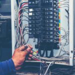 Electrician working on a circuit breaker panel with various wires.