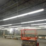Interior view of a large industrial warehouse with bright overhead lighting and machinery.