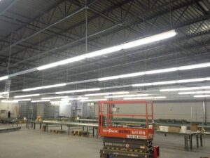 Interior view of a large industrial warehouse with bright overhead lighting and machinery.