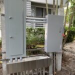 Two electrical panels mounted outside near a garden path.
