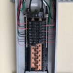 Open electrical panel with circuit breakers and copper bus bars.