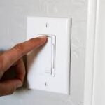 A hand adjusting a white wall dimmer switch.