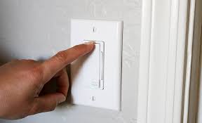 A hand adjusting a white wall dimmer switch.