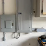 Electrical panels and wiring mounted on a wall in a utility space.