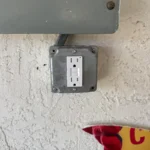 Electrical outlet mounted on a textured wall with a partial view of a colorful sign below.