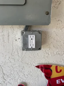 Electrical outlet mounted on a textured wall with a partial view of a colorful sign below.