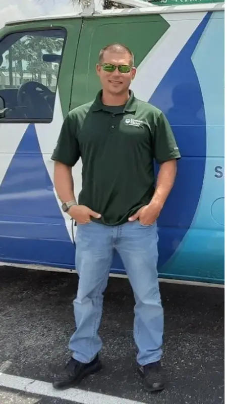A man in a green polo and jeans stands with hands in pockets outdoors.